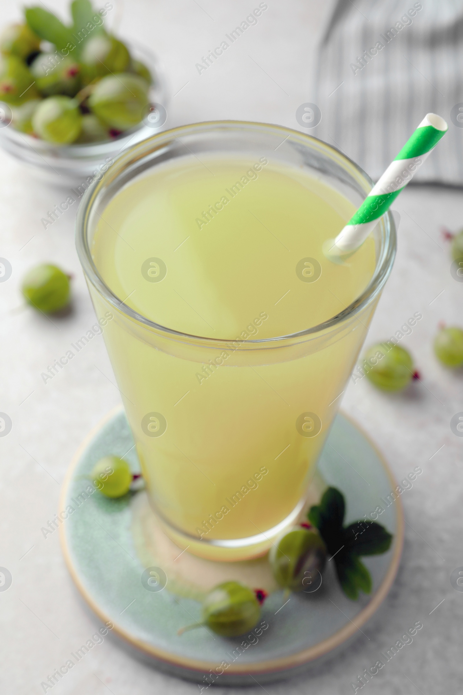 Photo of Tasty gooseberry juice in glass and fresh berries on light table, closeup