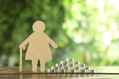 Photo of Pension savings. Figure of senior woman and stacked coins on wooden table outdoors