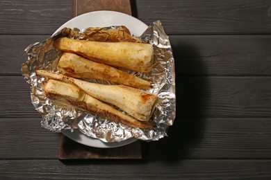 Tasty baked parsnips on black wooden table, top view