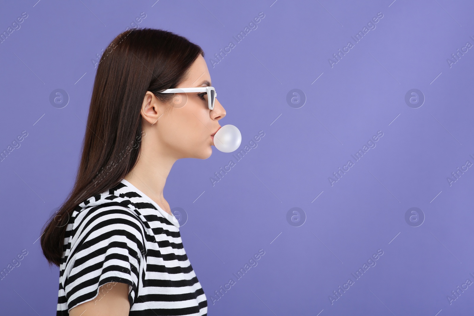 Photo of Beautiful woman in sunglasses blowing bubble gum on light purple background, space for text