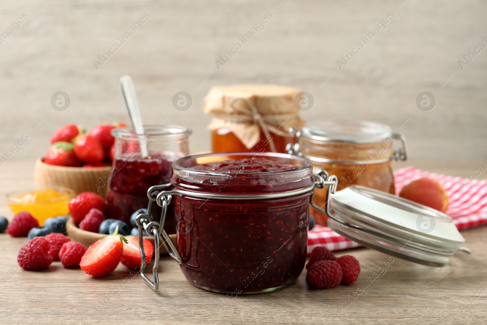 Photo of Jars with different jams and fresh fruits on wooden table