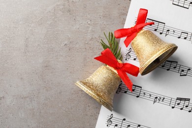 Photo of Golden shiny bell with red bow and music sheet on light table, flat lay. Space for text. Christmas decoration