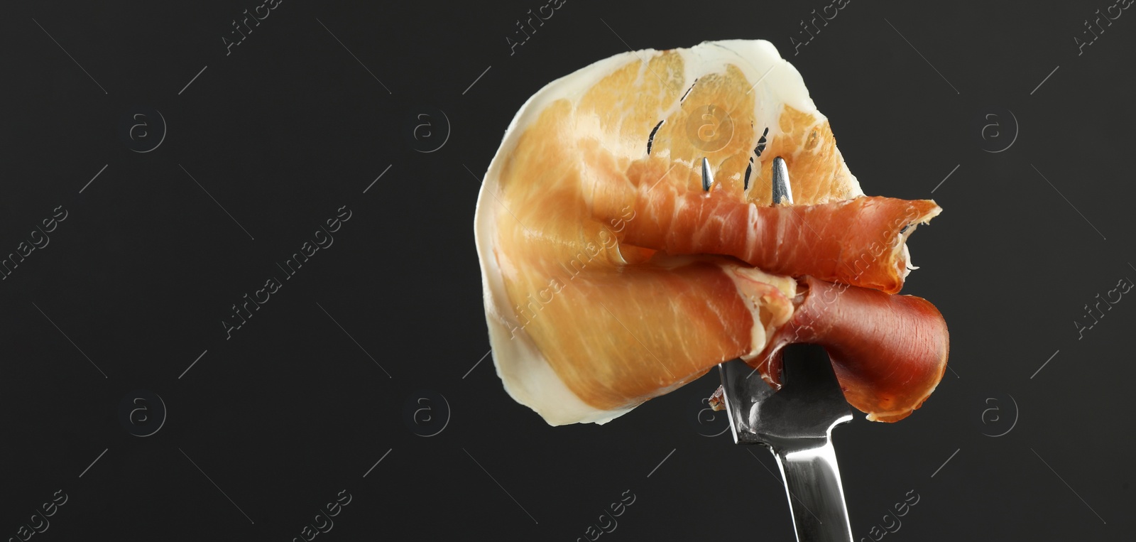 Photo of Fork with slice of tasty jamon on black background, closeup. Space for text