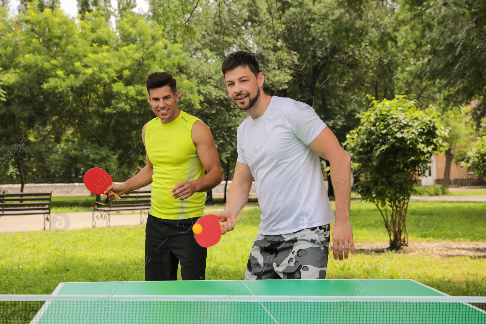 Photo of Men playing ping pong in park on summer day