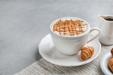 Cup of caramel macchiato with tasty pastry on table. Space for text