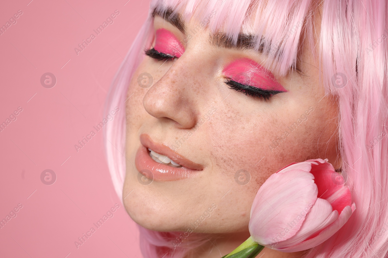 Photo of Beautiful woman with bright makeup, fake freckles and tulip on pink background, closeup