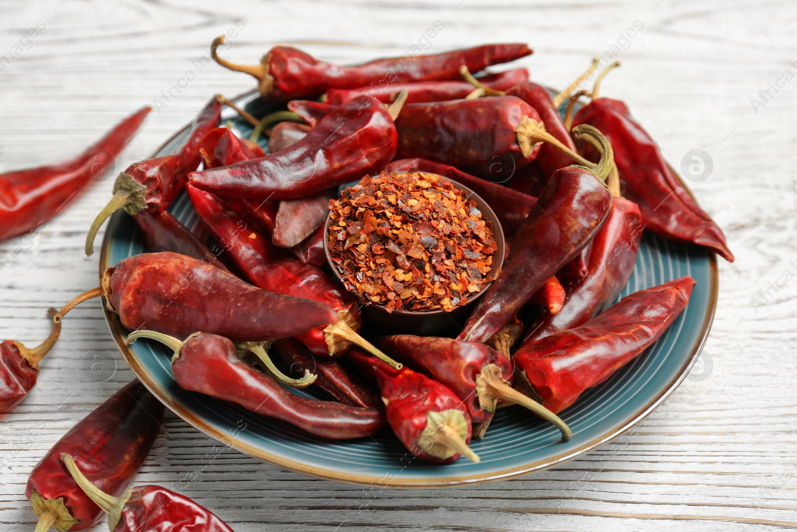 Photo of Plate with dry chili peppers and powder on wooden background