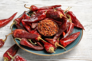 Plate with dry chili peppers and powder on wooden background