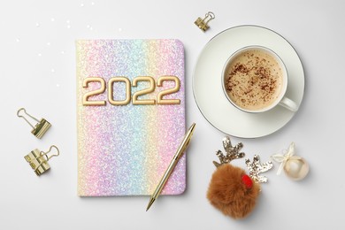 Stylish planner, cup of aromatic coffee and Christmas decor on white background, flat lay. 2022 New Year aims