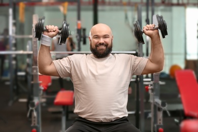 Photo of Overweight man training with dumbbells in gym