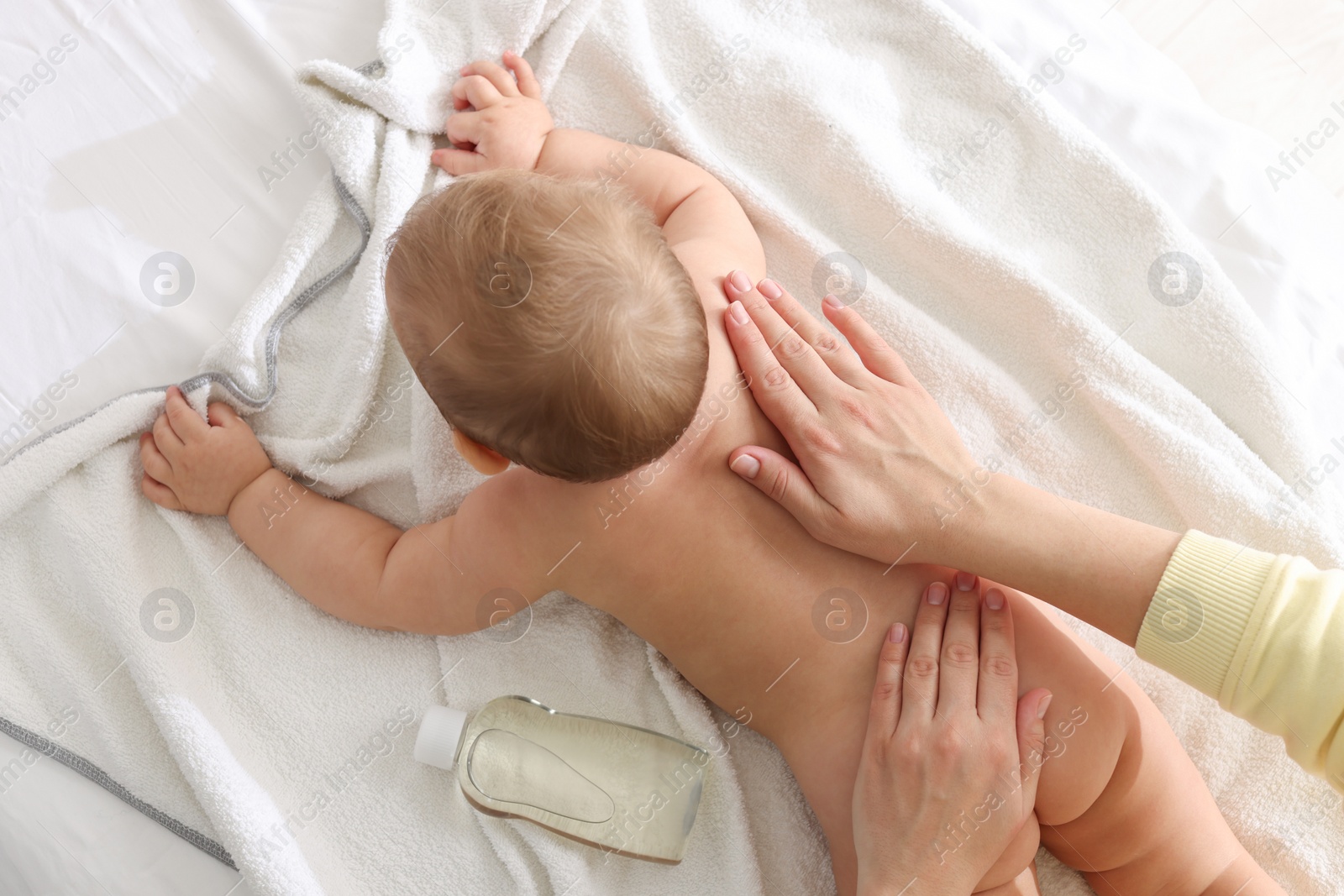 Photo of Mother massaging her baby with oil on towel after bathing, top view