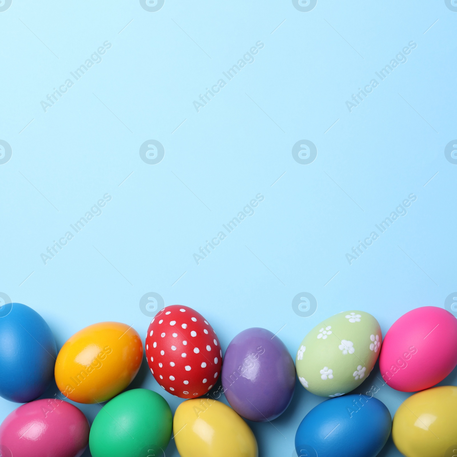 Photo of Bright painted eggs on light blue background, flat lay with space for text. Happy Easter