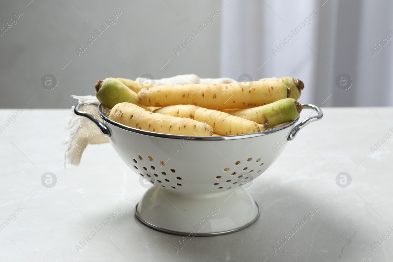 Photo of Raw white carrots in colander on light grey table