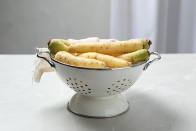 Raw white carrots in colander on light grey table