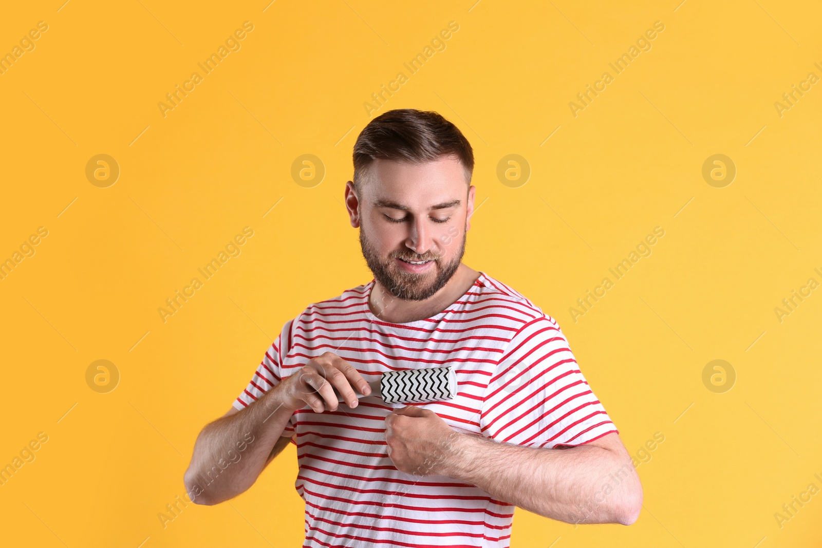 Photo of Young man cleaning clothes with lint roller on yellow background