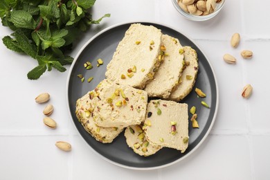 Photo of Tasty halva with pistachios and mint on white tiled table, flat lay