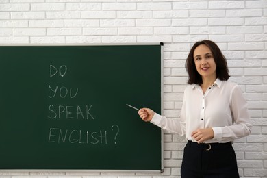 Photo of Teacher near green chalkboard with inscription Do You Speak English? in classroom