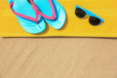 Photo of Yellow towel, sunglasses and flip flops on sand, top view with space for text