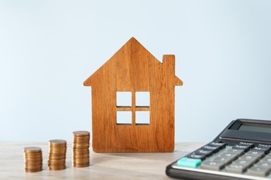 Photo of House model, calculator and coins on wooden table against light blue background