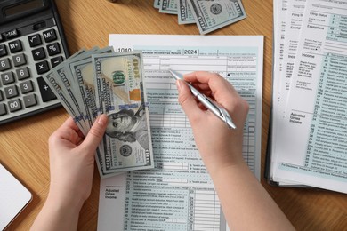Photo of Payroll. Woman with dollar banknotes working with tax return forms at wooden table, top view