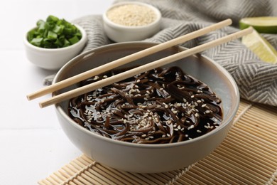 Photo of Tasty buckwheat noodles (soba) with sauce in bowl and chopsticks on white table, closeup