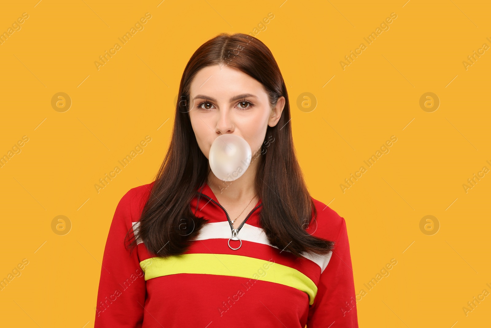 Photo of Beautiful woman blowing bubble gum on orange background