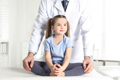 Photo of Professional orthopedist examining little girl in clinic