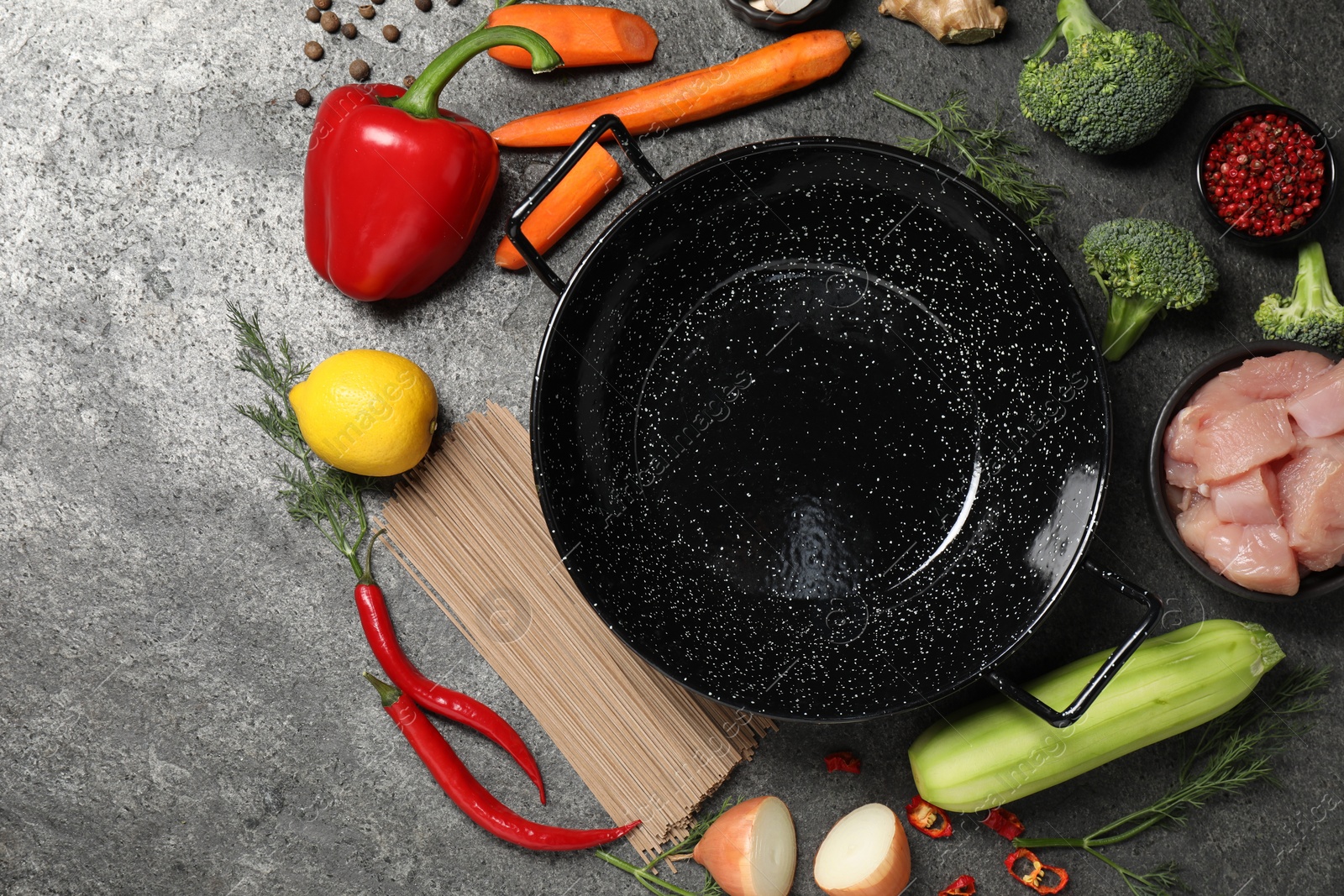 Photo of Empty iron wok surrounded by ingredients on grey table, flat lay