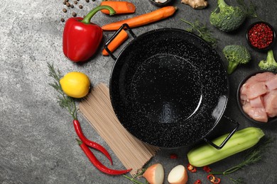 Empty iron wok surrounded by ingredients on grey table, flat lay