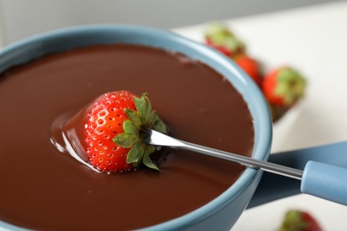 Dipping strawberry into fondue pot with chocolate, closeup