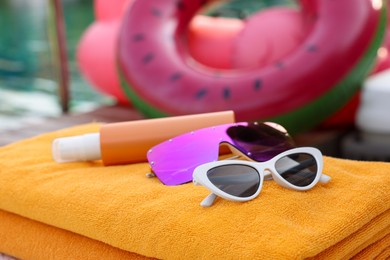 Photo of Beach towels, sunglasses and sunscreen on sunbed near outdoor swimming pool, closeup. Luxury resort