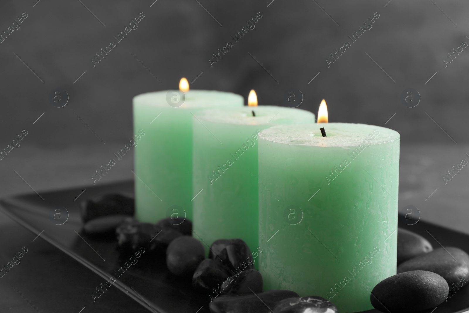 Photo of Dark plate with three burning candles and rocks on table