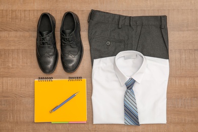 School uniform for boy and notebook on wooden background, top view