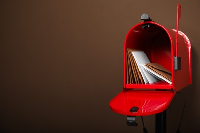 Photo of Open red letter box with envelopes against brown background. Space for text