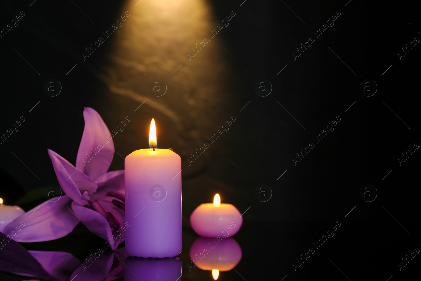 Image of Violet lily and burning candles on black mirror surface in darkness, space for text. Funeral attributes