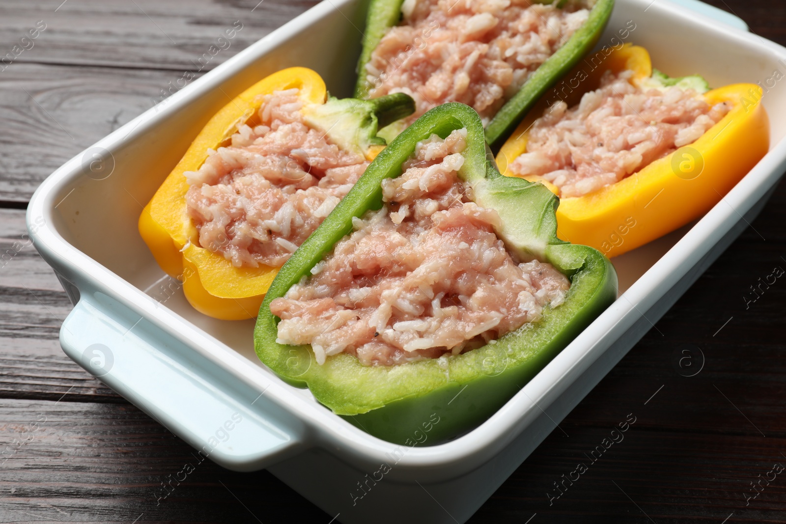 Photo of Raw stuffed peppers in dish on wooden table, closeup