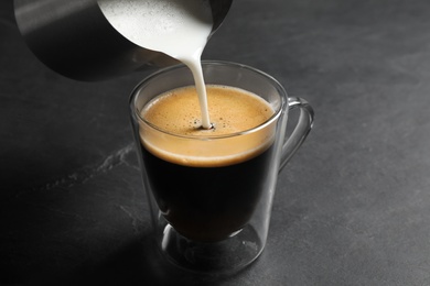 Photo of Pouring milk into cup of coffee on black table