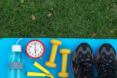 Alarm clock and morning exercise set on green grass, flat lay. Space for text