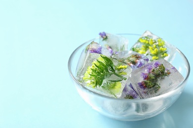 Bowl of ice cubes with flowers on blue background. Space for text