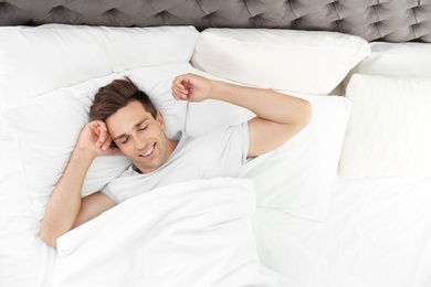 Photo of Young man waking up in bed with pillows at home