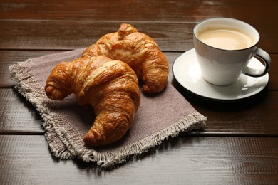 Photo of Delicious fresh croissants and cup of coffee on wooden table