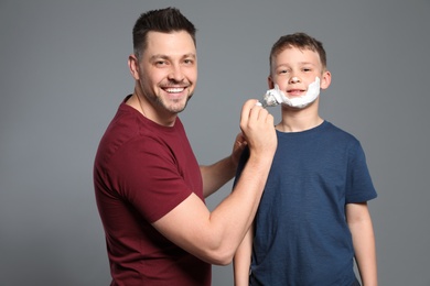 Dad applying shaving foam on son's face, grey background