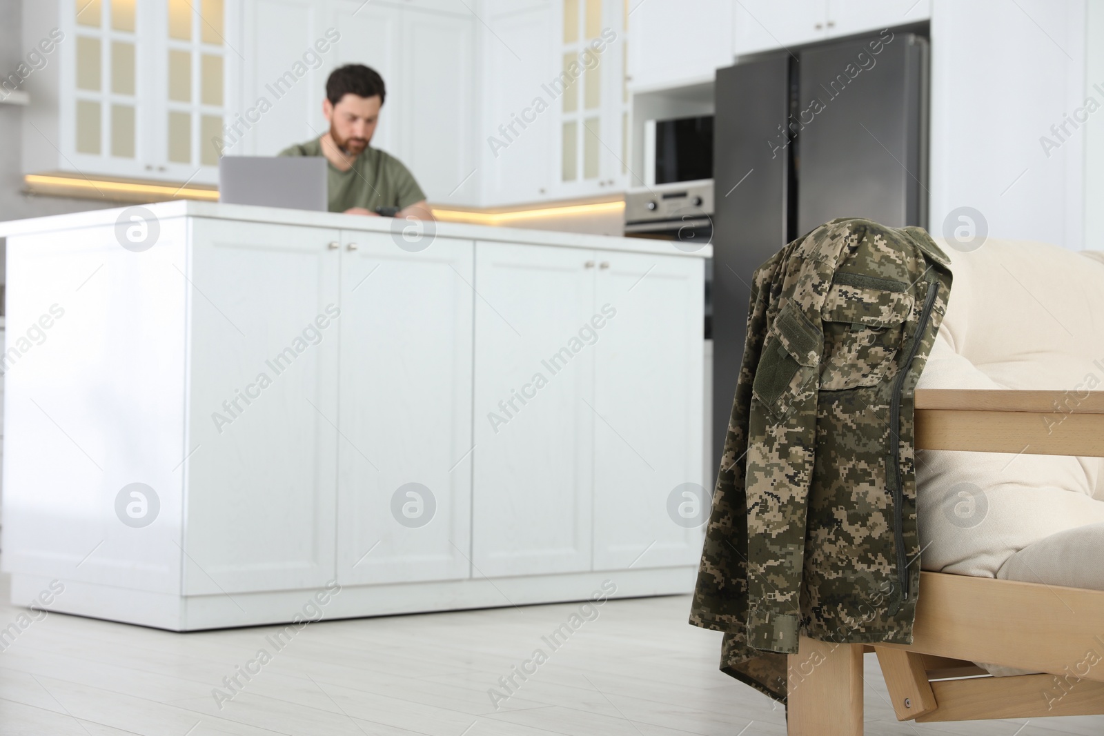 Photo of Soldier using laptop at table in kitchen, focus on uniform. Military service