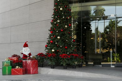 Photo of Funny Santa Claus, wrapped gifts and Christmas tree near building. Festive outdoor decoration