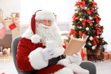 Authentic Santa Claus with glass of milk reading book indoors