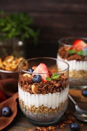 Photo of Tasty granola with berries, nuts, yogurt and chia seeds in glass on table