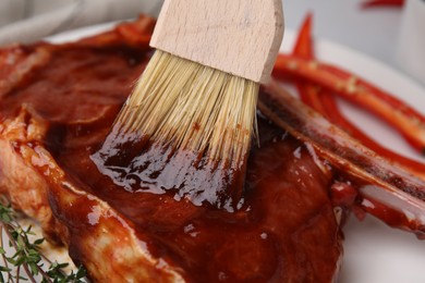 Photo of Spreading marinade onto raw meat with basting brush on plate, closeup