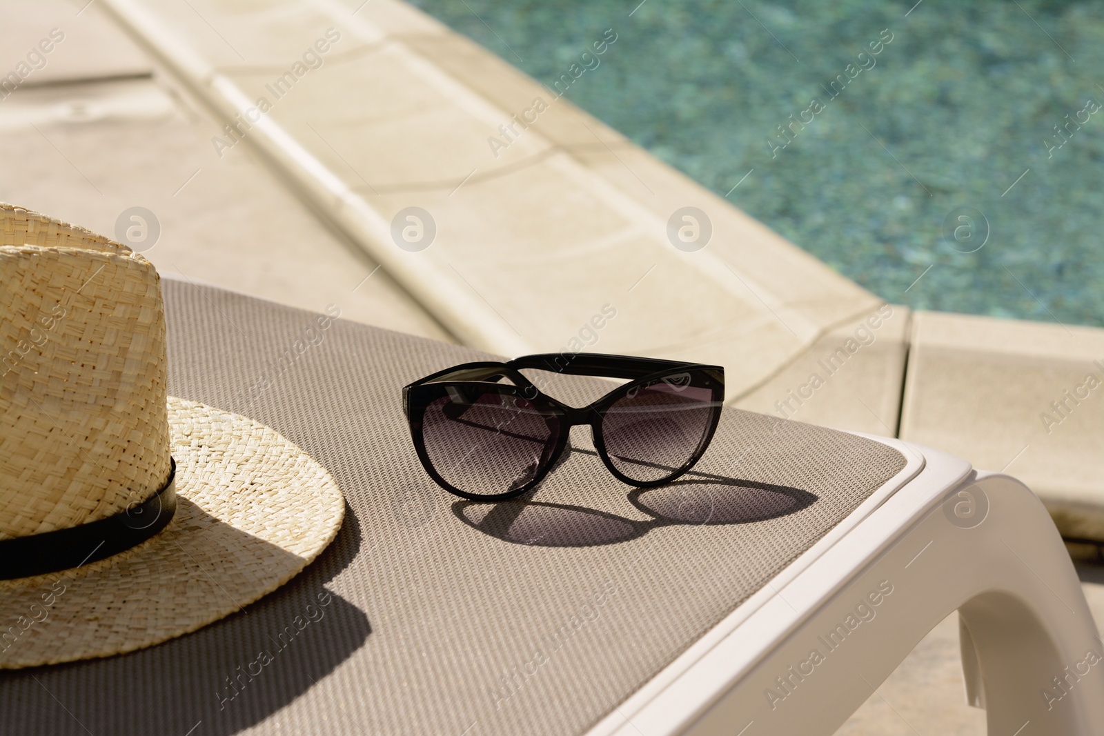 Photo of Stylish straw hat and sunglasses on grey sunbed near outdoor swimming pool