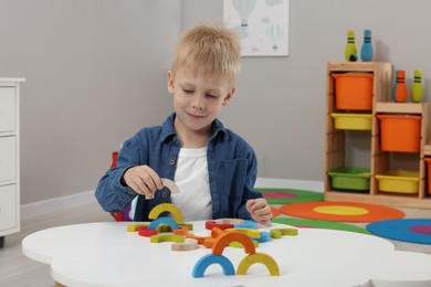 Photo of Motor skills development. Boy playing with colorful wooden arcs at white table in kindergarten