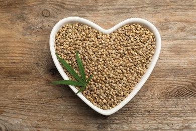 Photo of Organic hemp seeds and leaf on wooden background, top view